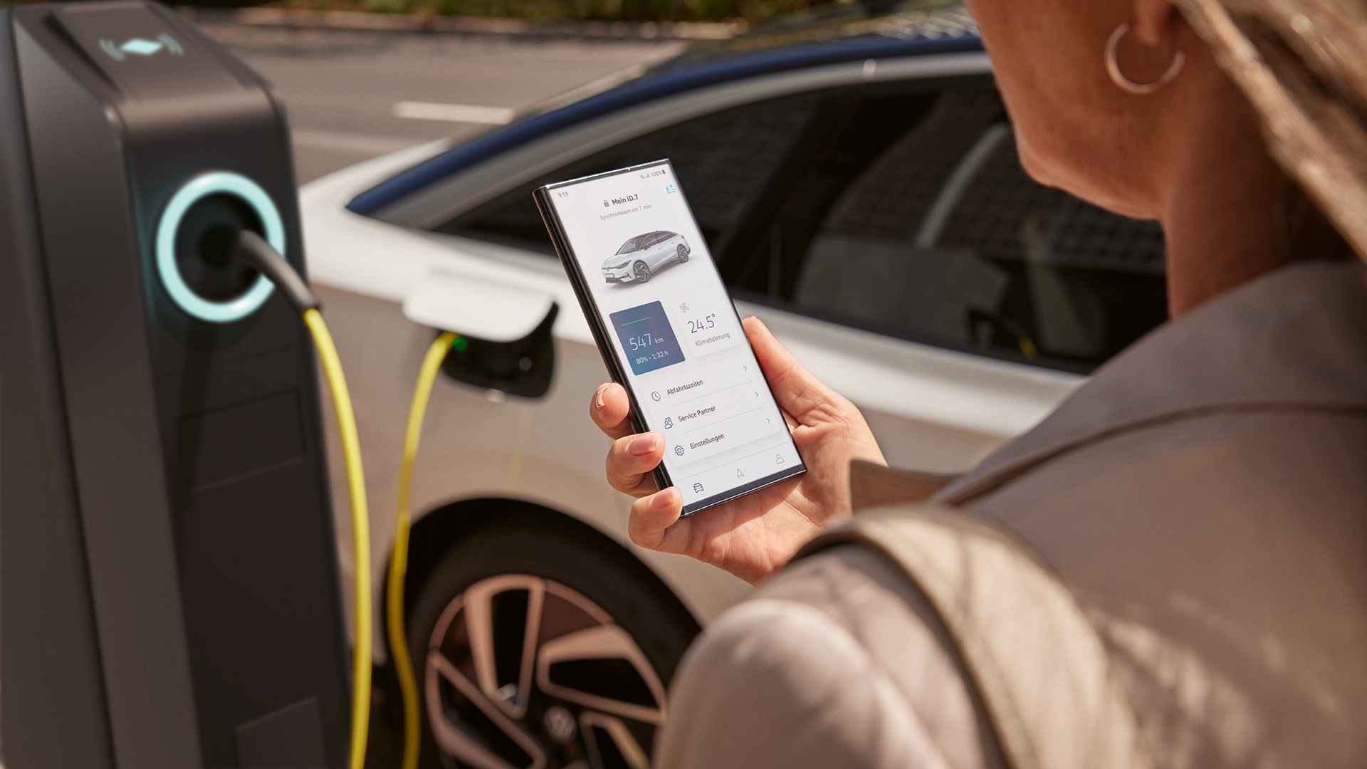 VW ID.7 wird geladen, Frau verfolgt Ladestatus am Handy